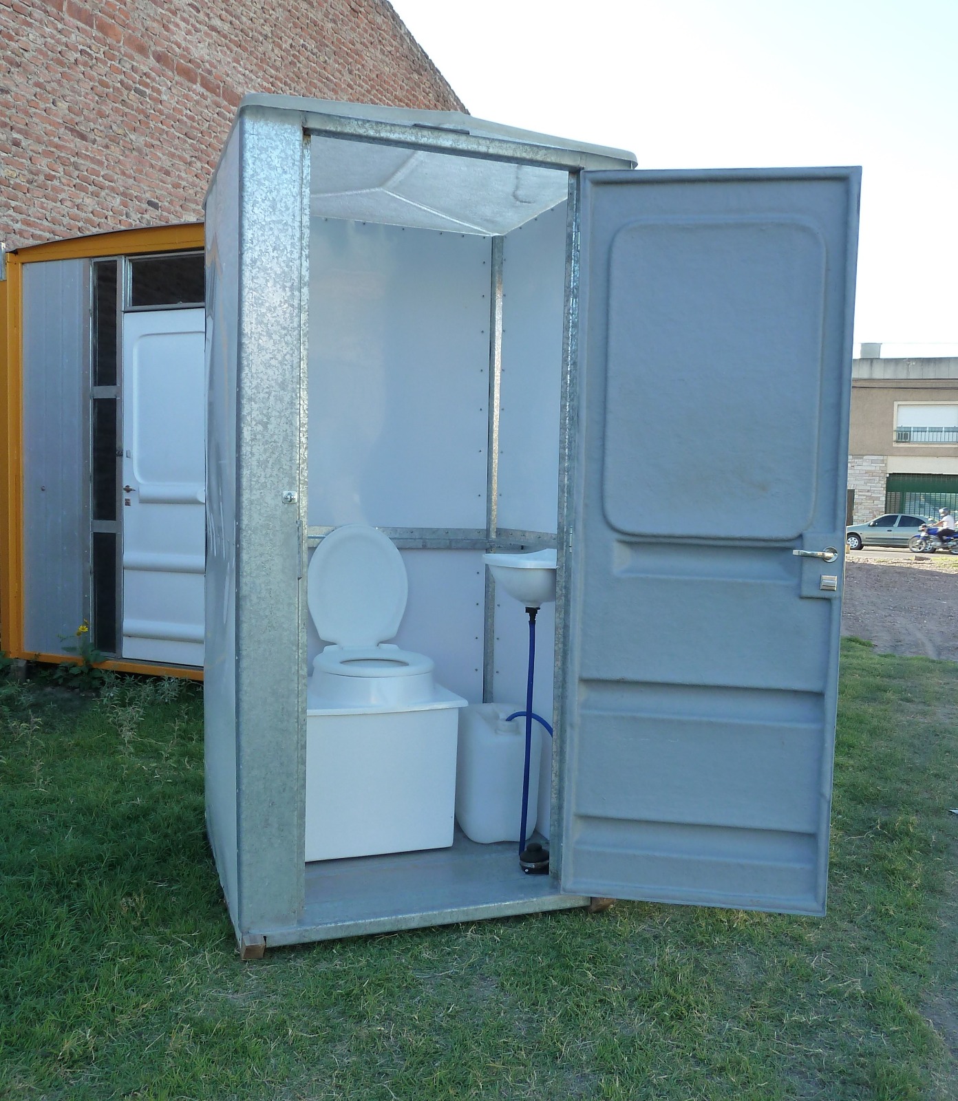 Baño químico portátil abierto con inodoro, lavamanos y accesorios interiores visibles