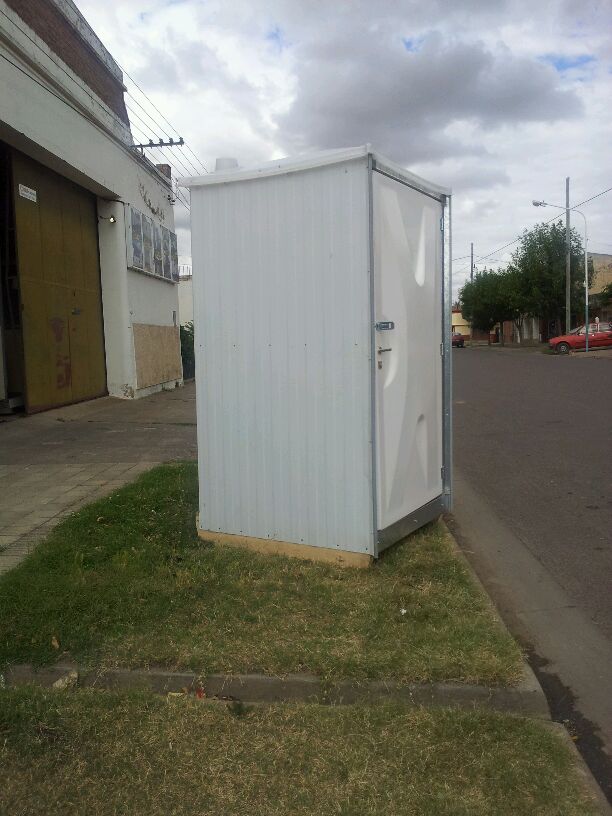 Baño químico portátil blanco cerrado instalado sobre vereda en vista exterior lateral